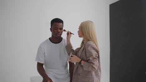 A-female-make-up-artist-makes-makeup-at-a-professional-photo-shoot-of-a-football-player.-Photo-studio-with-professional-equipment-and-team-of-workers.-team-discussing-direction-for-production